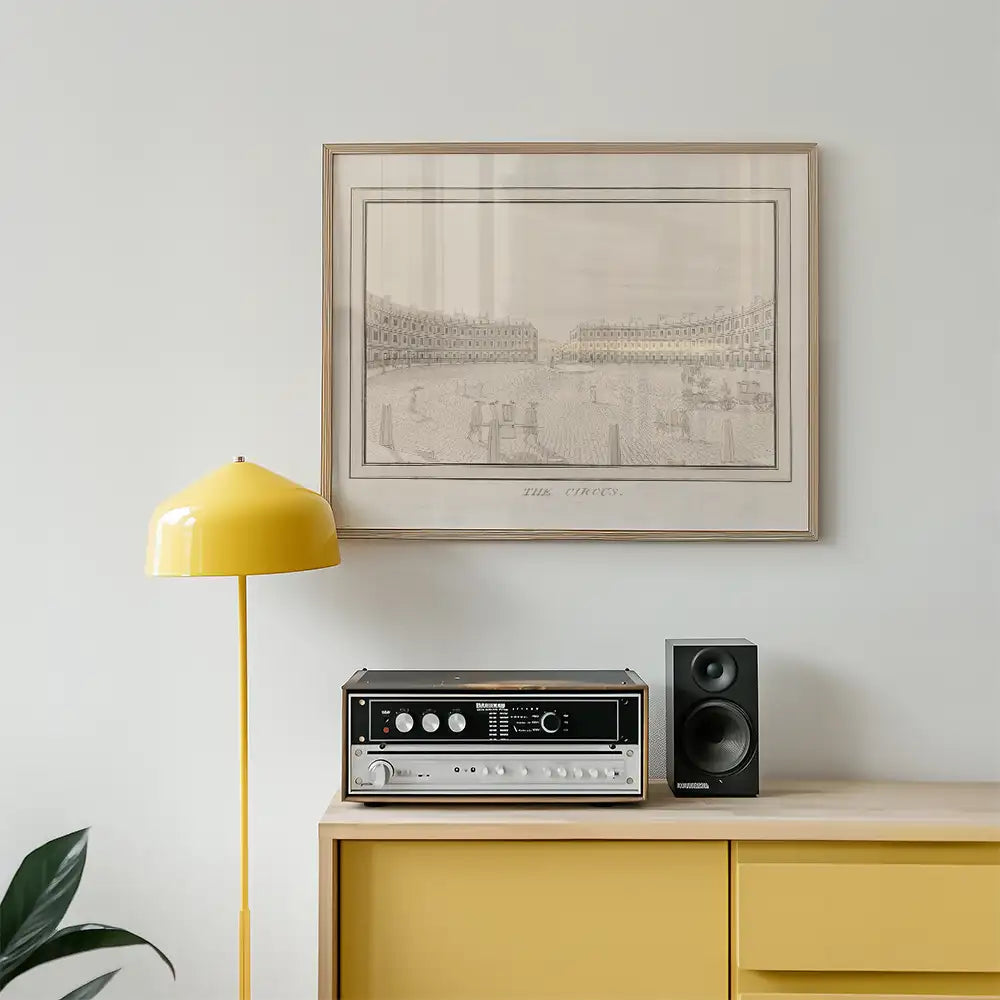Framed vintage illustration of a circus scene hanging above a yellow lamp and audio equipment on a wooden cabinet.