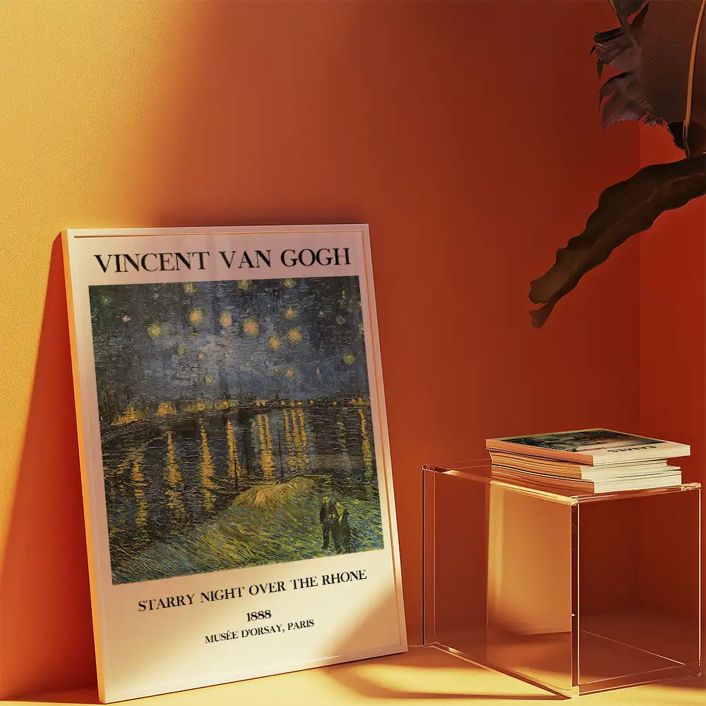 Vincent Van Gogh Starry Night Over the Rhone poster displayed against an orange wall with a clear side table holding a stack of books.