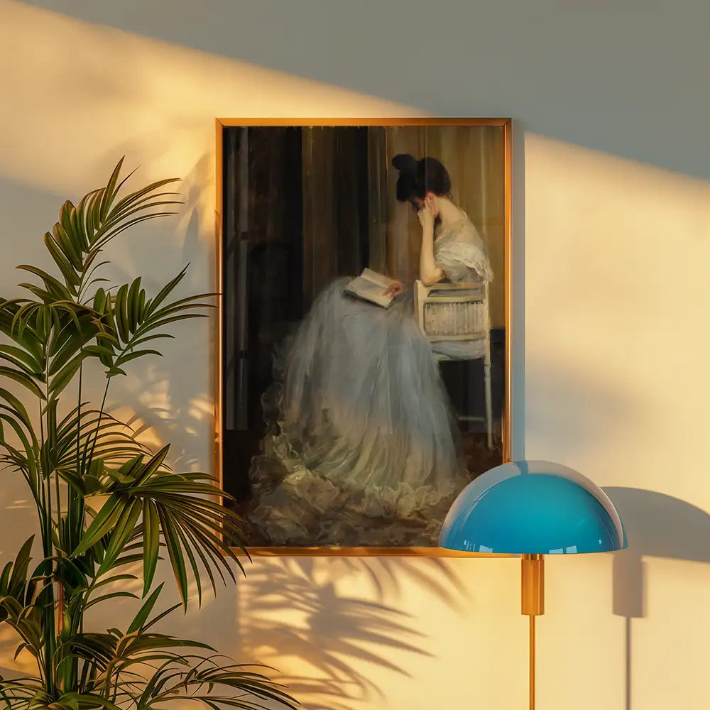 Painting of a woman in a flowing dress reading a book, framed and displayed in a softly lit room with a plant and a modern lamp.