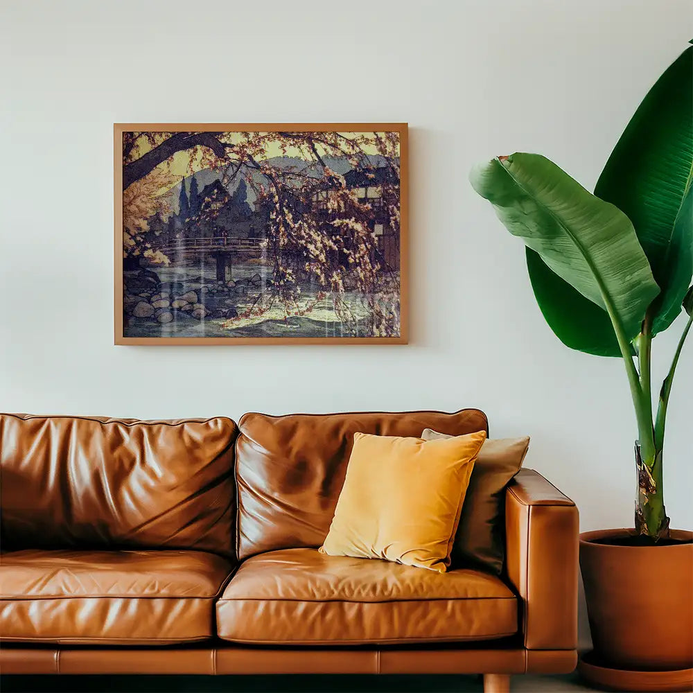 Framed painting depicting a serene landscape with a bridge and willow trees, displayed above a brown leather sofa in a cozy living room setting.