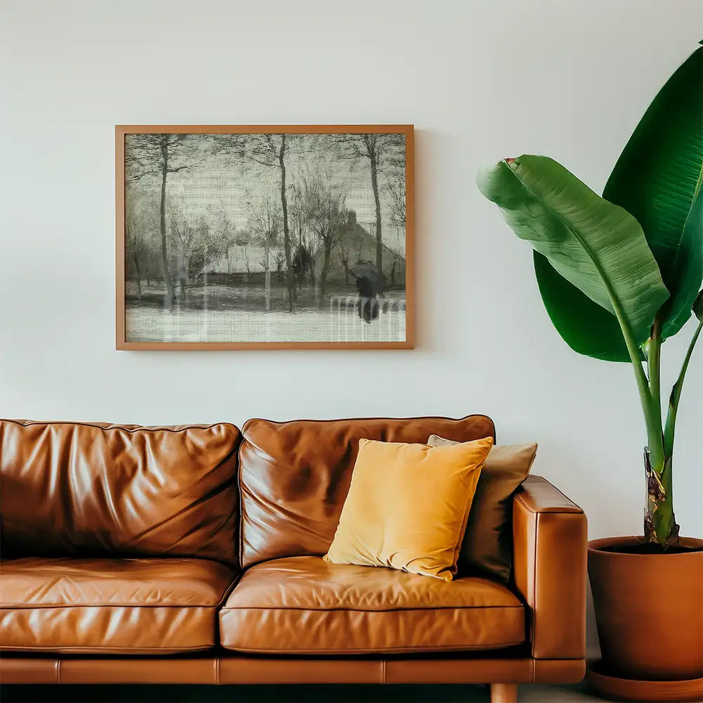 Framed black and white painting of a landscape with trees and a house, displayed above a brown leather sofa with a yellow cushion and large green plant.