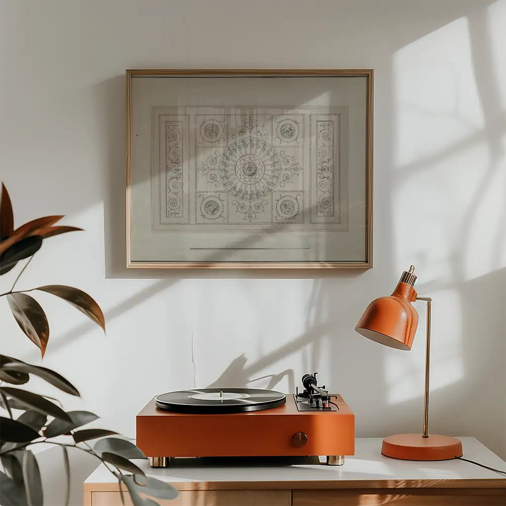 A vintage-style framed artwork hanging above an orange turntable and desk lamp in a well-lit room with a plant in the foreground.