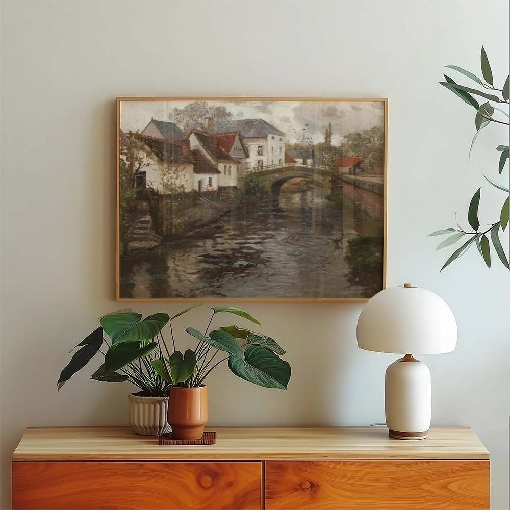 A serene painting of a picturesque canal scene with charming houses and a bridge, framed and displayed on a wall above a wooden side table adorned with a potted plant and a stylish lamp.