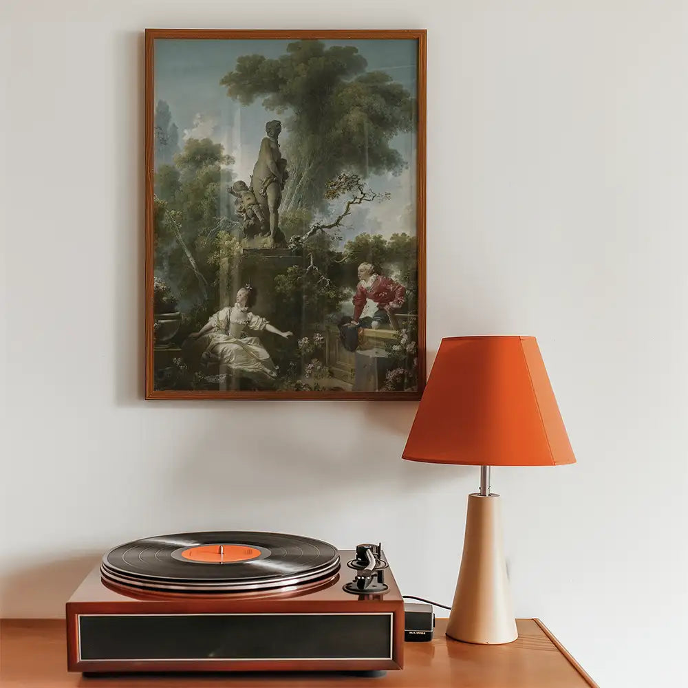 Framed painting of a classical scene hung on a wall above a vintage record player and an orange table lamp.