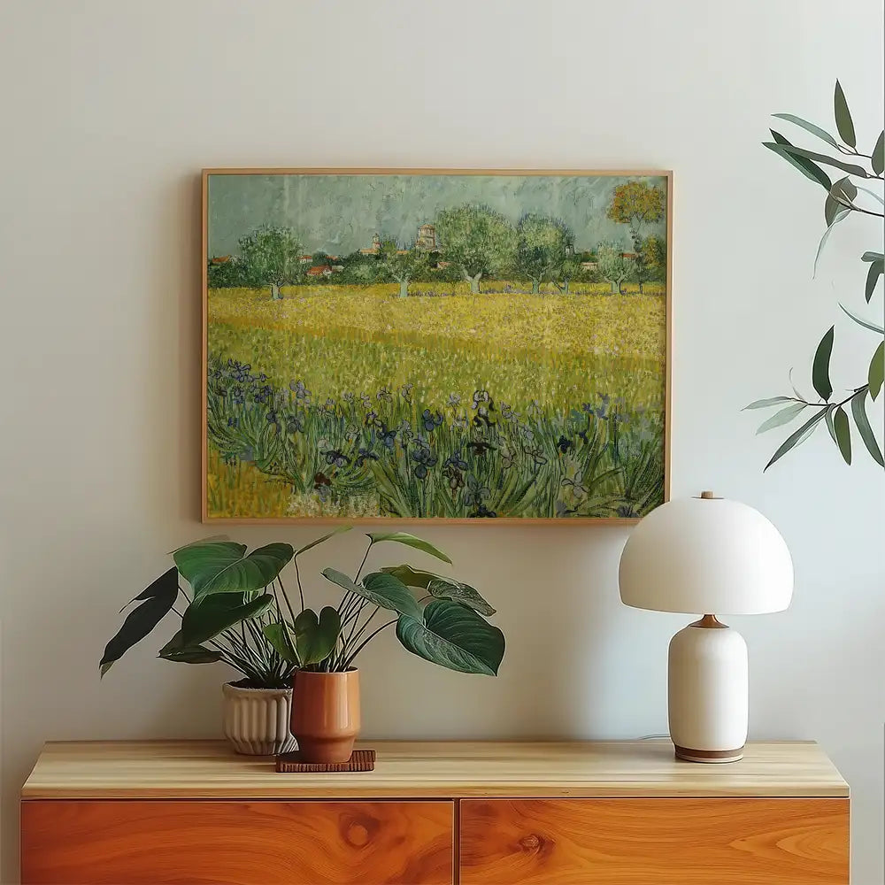Framed painting of a vibrant yellow field with trees and blue flowers, displayed above a wooden sideboard with a potted plant and a white lamp.