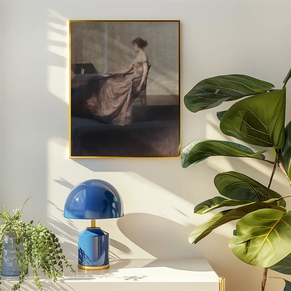 Framed painting of a woman in a pink dress sitting at a desk, displayed on a wall with a blue lamp and decorative plant nearby.
