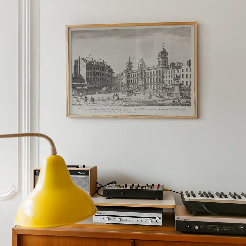 Framed vintage illustration of a bustling urban scene, hung on a white wall above a retro audio setup and a bright yellow lamp.