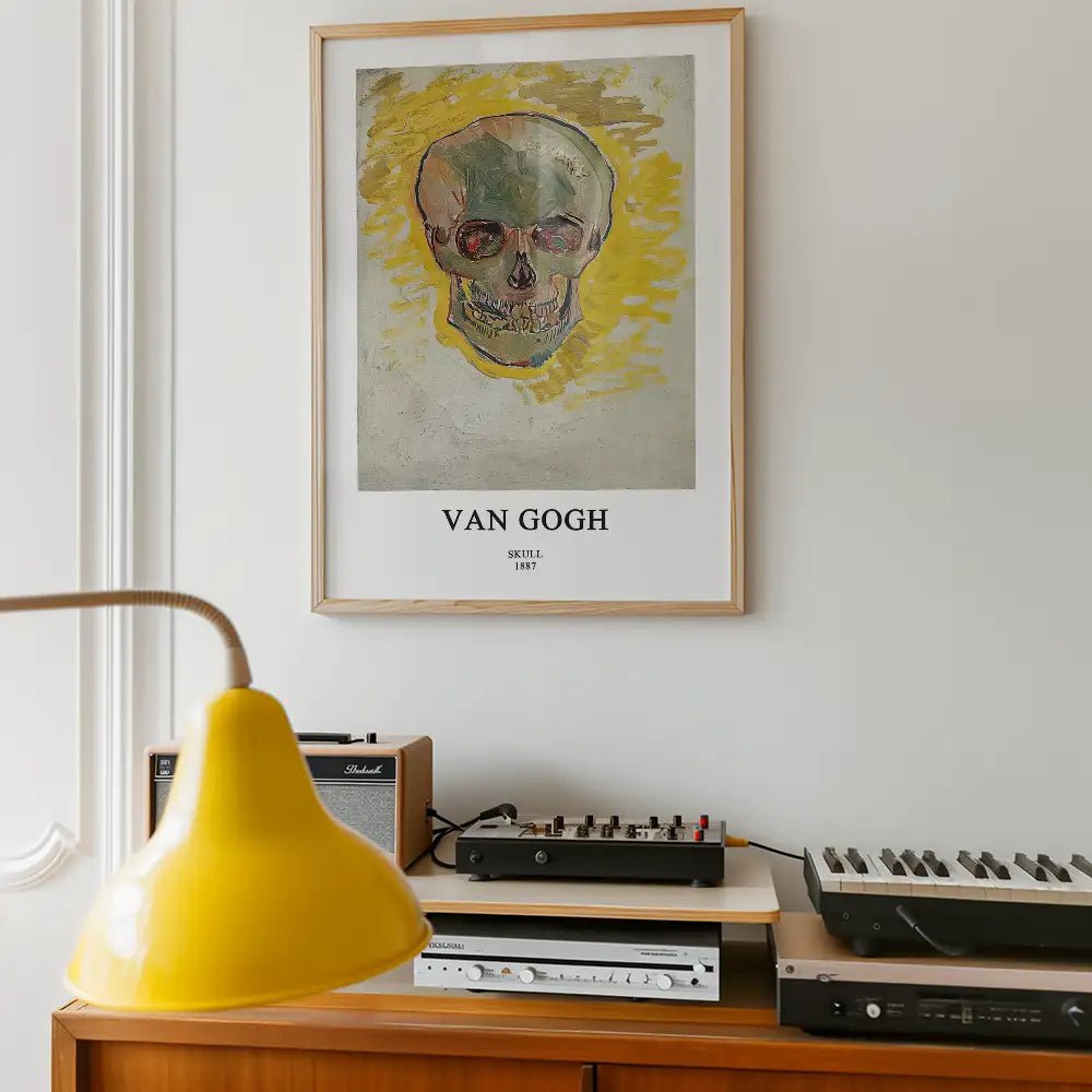 Framed poster of Vincent van Gogh's "Skull" from 1887, featuring a vibrant skull illustration against a yellow background, displayed in a modern interior with audio equipment and a yellow lamp.