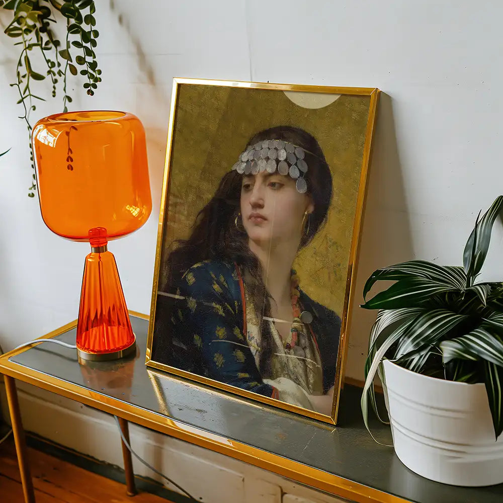 Framed painting of a woman with a headdress, displayed on a table next to an orange lamp and a potted plant.