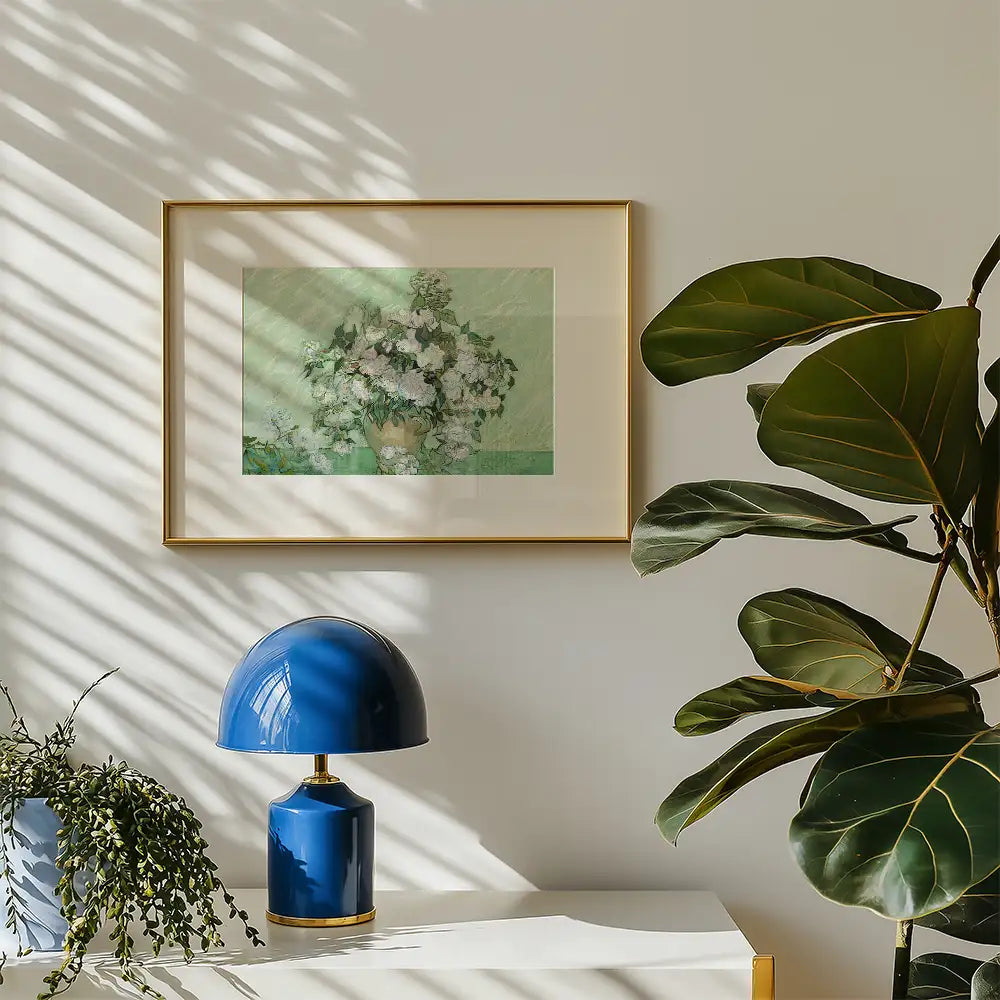 A framed painting of a bouquet of flowers in a vase, displayed on a wall beside a blue lamp and a plant in a bright room with sunlight and shadows.