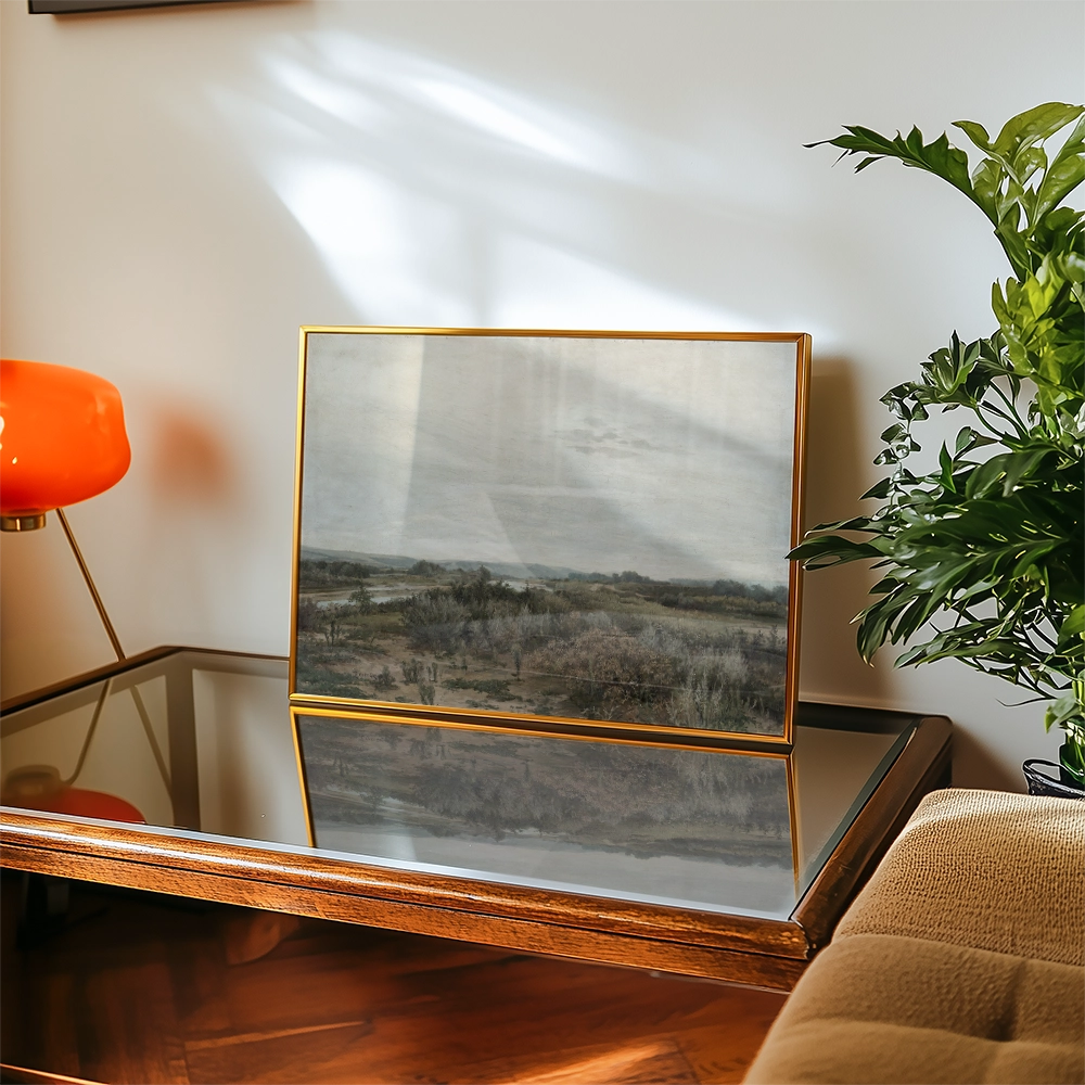 Framed landscape painting on a coffee table with a modern lamp and a plant in the background.