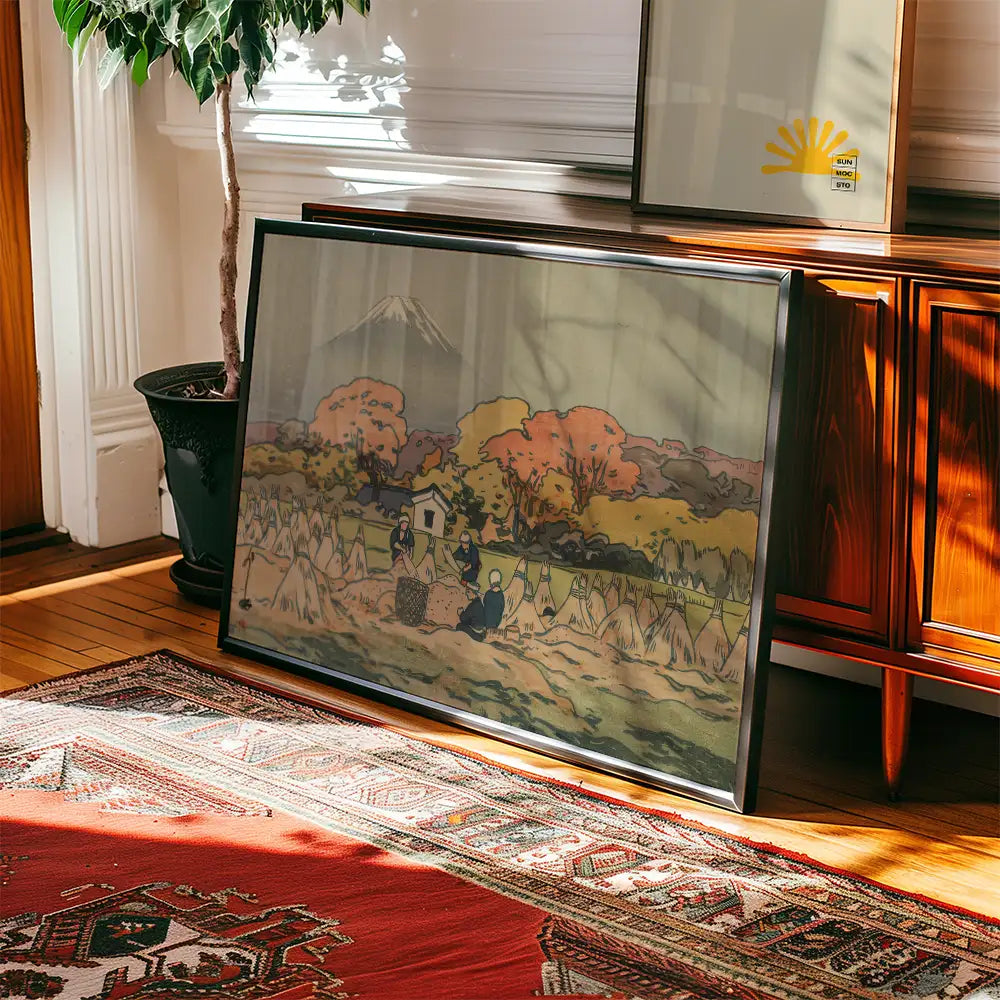 Framed painting depicting a serene landscape with colorful autumn trees, a small house, and figures working in a field, placed on a wooden floor beside a plant.