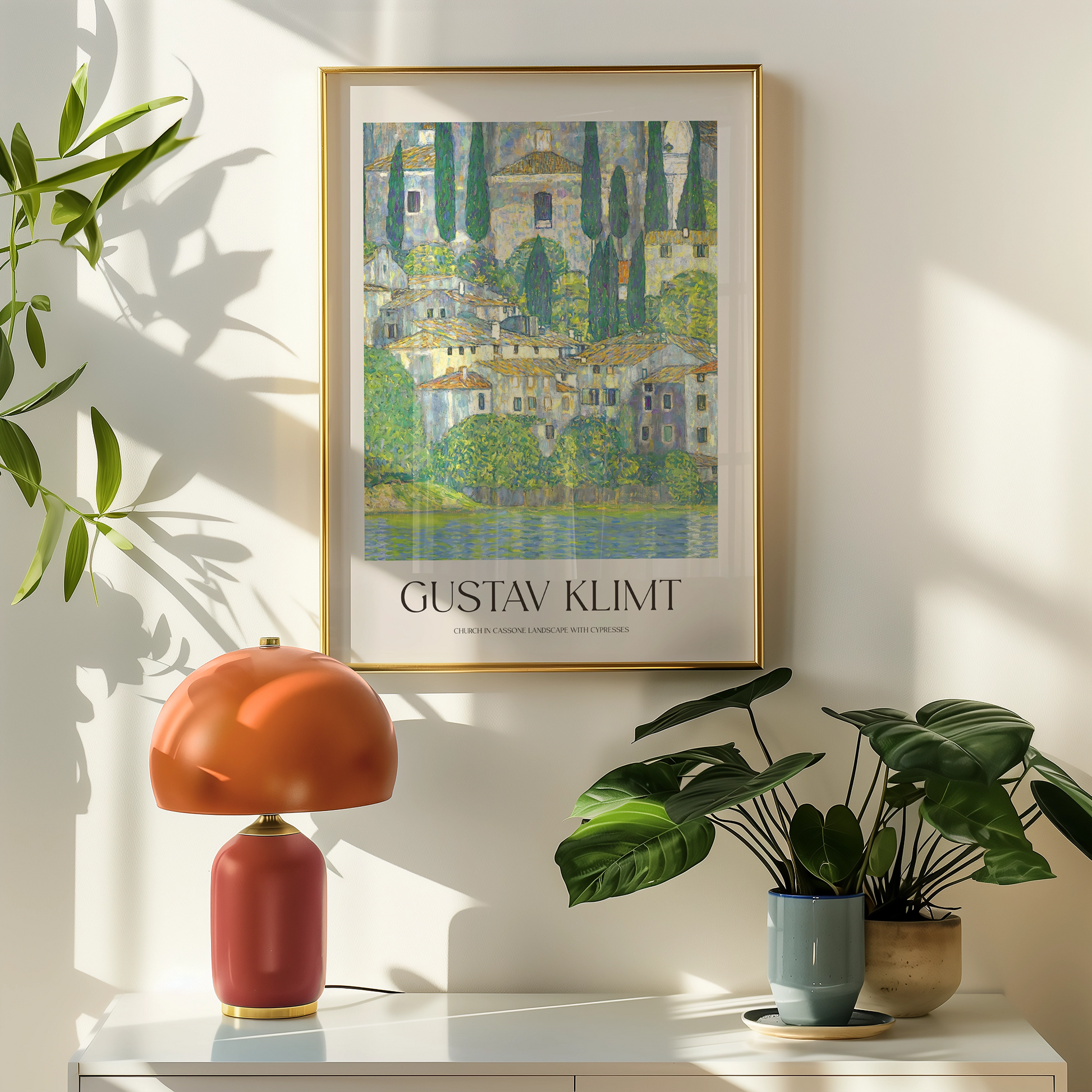 Framed Gustav Klimt painting titled "Church in Cassone Landscape with Cypresses" displayed on a wall next to a modern lamp and potted plants.