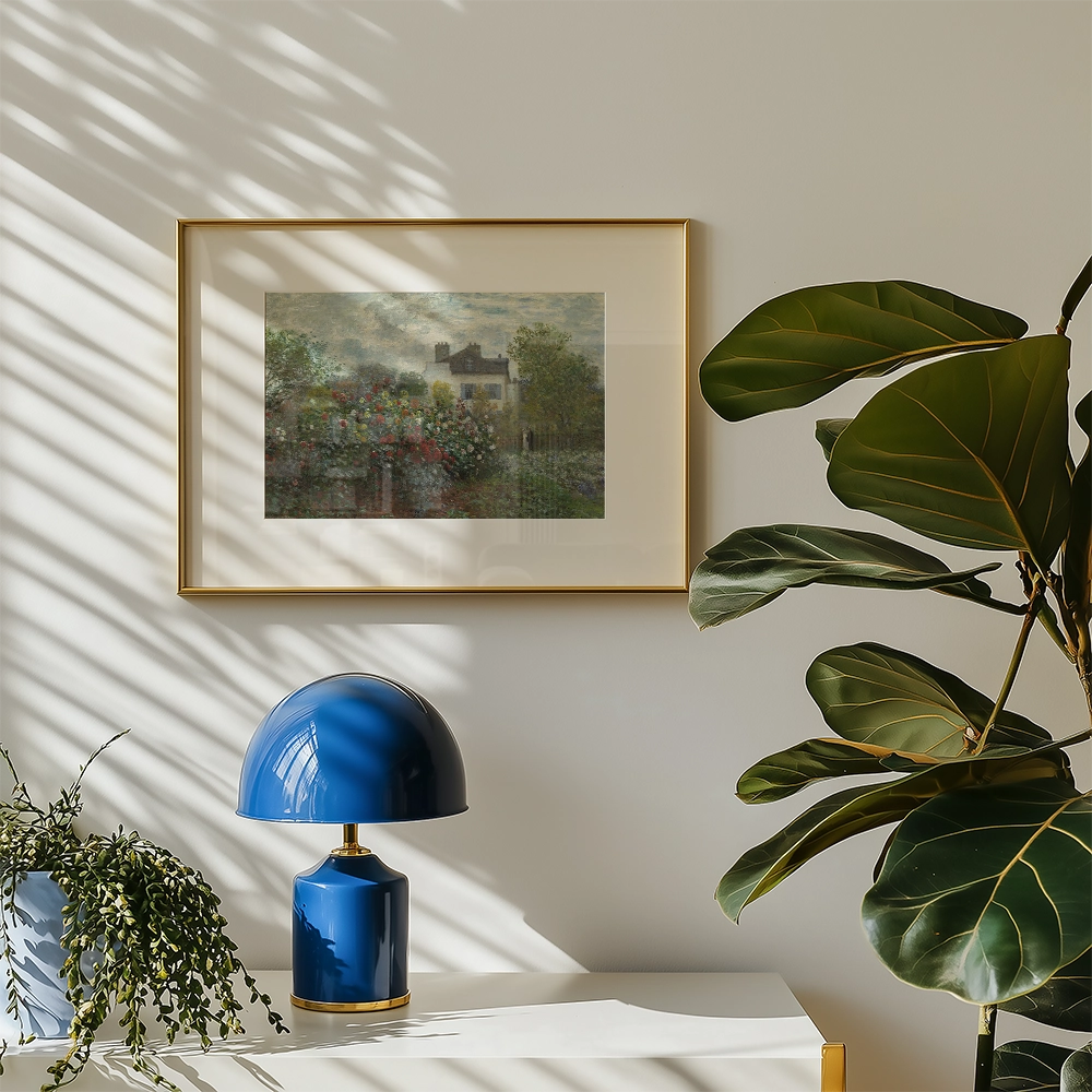 Framed painting of a house surrounded by colorful flowers on a wall in a bright room with a blue lamp and green plant.