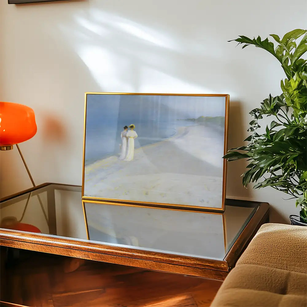 Framed painting of two figures standing on a beach, displayed on a wooden table with a modern lamp and a plant in a contemporary interior setting.