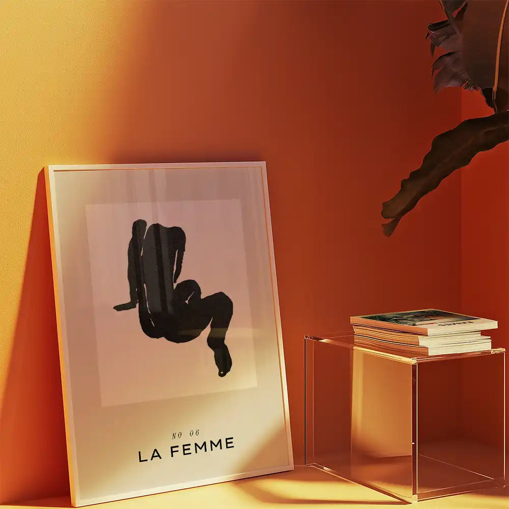 Modern poster print of a famous painting titled "La Femme," featuring a stylized black silhouette figure against a light background, displayed in a contemporary setting with warm orange walls and minimalist décor.