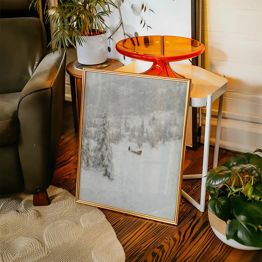 Framed painting of a snowy landscape leaning against a chair in a cozy living room setting.