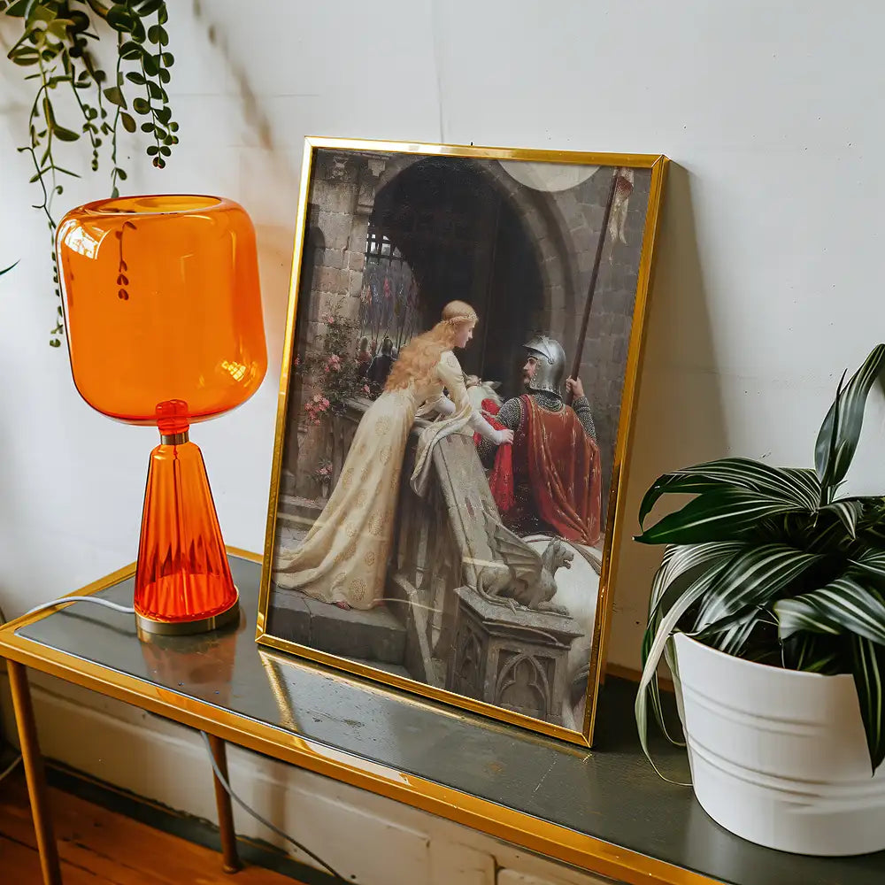 A framed painting depicting a romantic scene between a knight and a lady, set against a stone backdrop, positioned next to an orange lamp and surrounded by indoor plants.