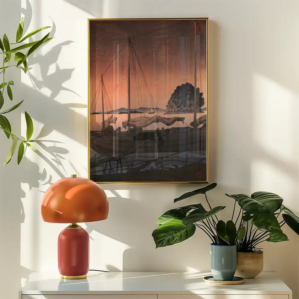 A serene painting of sailboats at sunset, framed in gold, displayed on a white wall with a modern lamp and potted plants in a bright room.