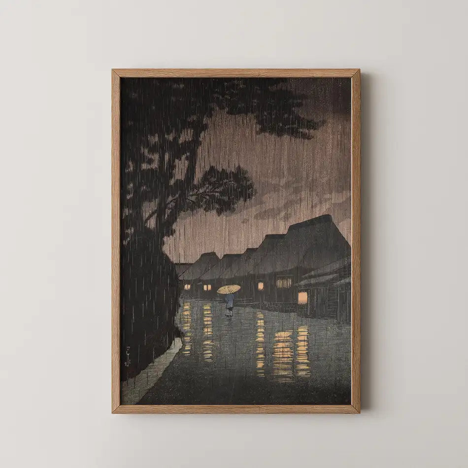 Framed painting depicting a rainy night scene with a person holding an umbrella walking by illuminated houses and reflections on a wet street.