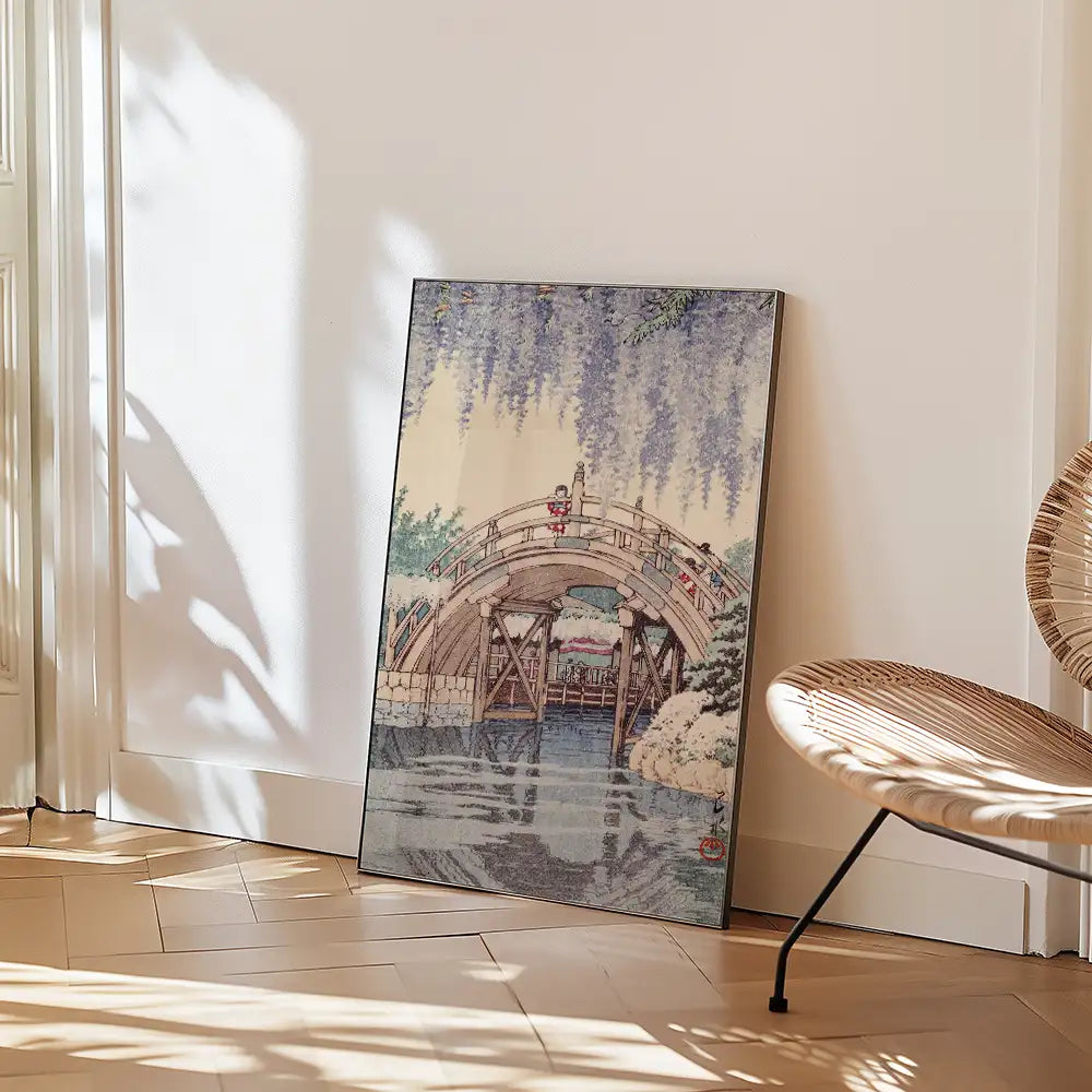 Painting of a bridge surrounded by wisteria trees, resting against a wall in a cozy interior setting.