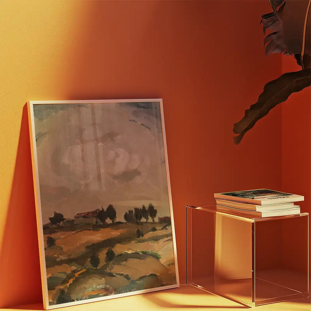 Framed landscape painting propped against an orange wall, with a clear acrylic table and stacked books beside it.
