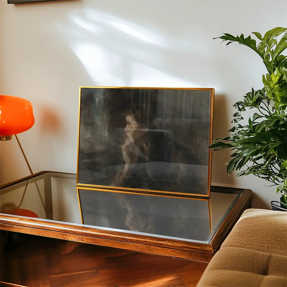 Framed painting displayed on a coffee table with an orange lamp and greenery in a cozy setting