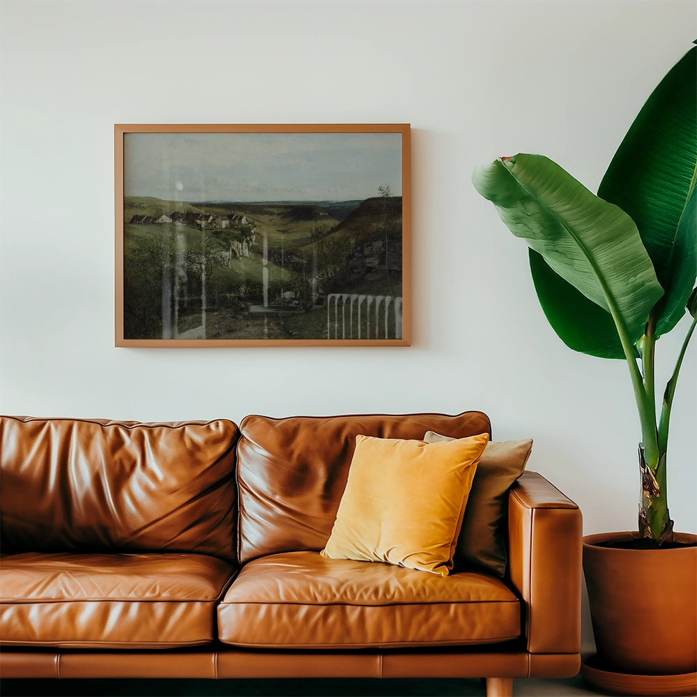 Framed painting of a serene landscape depicting hills and a cloudy sky, displayed above a brown leather couch with cushions, alongside a green plant in a pot.