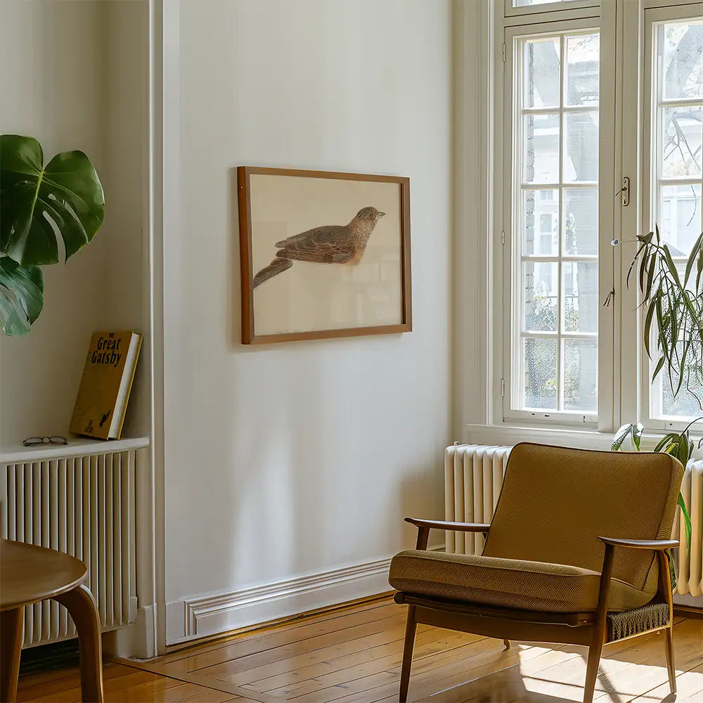 Framed artwork of a bird displayed on a wall in a modern living room with a cozy chair and plants.