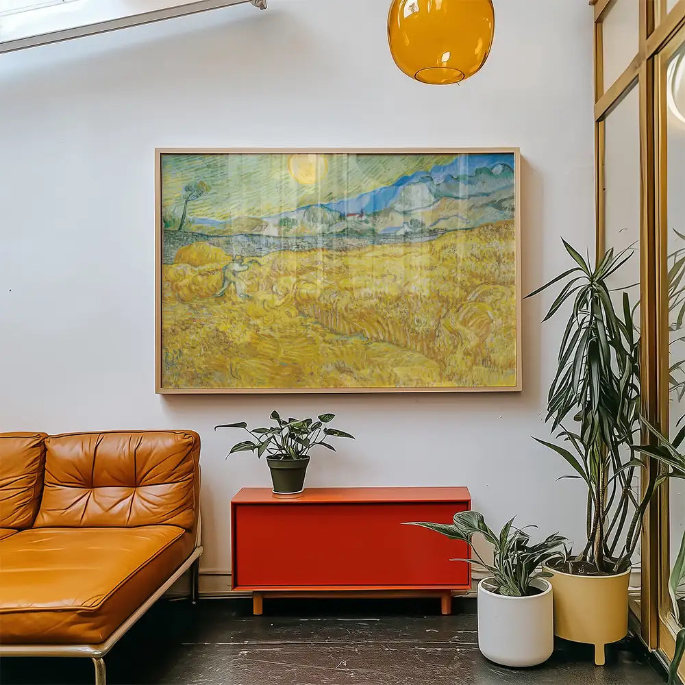 Framed painting of a wheat field with a figure, displayed in a modern living room with a brown couch and potted plants.
