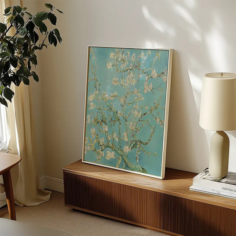 Painting of a blossoming tree in a blue background, displayed next to a lamp and a wooden shelf in a bright room.