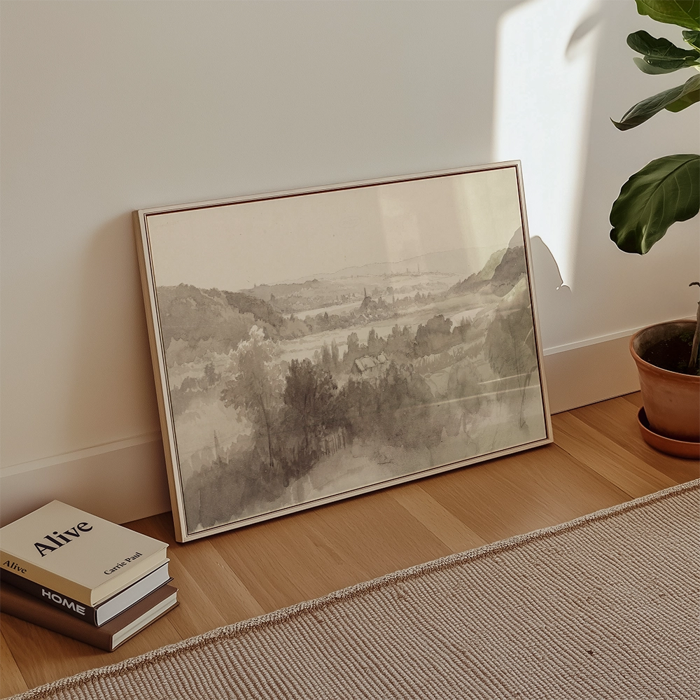 Framed landscape painting in muted tones leaning against a wall next to books and a potted plant.