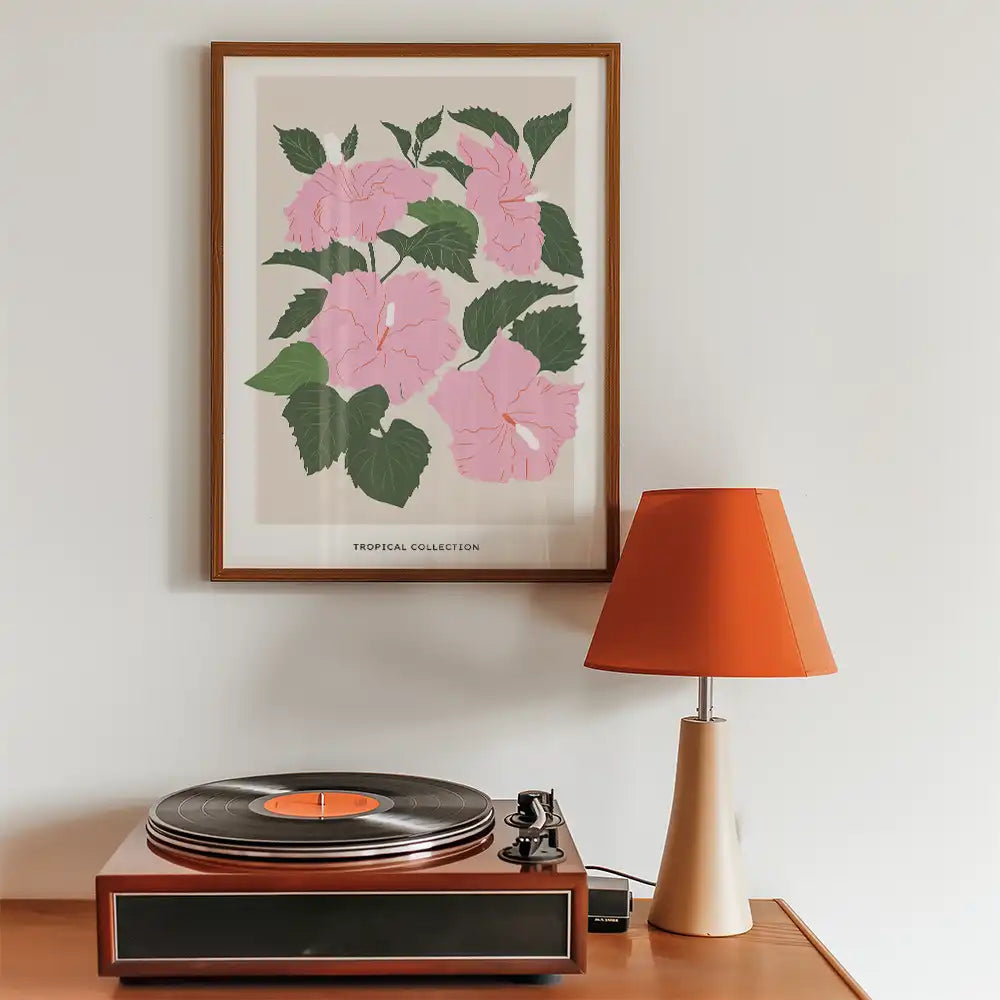 Modern tropical floral poster featuring pink hibiscus flowers and green leaves, framed and displayed above a vintage record player and orange lamp.