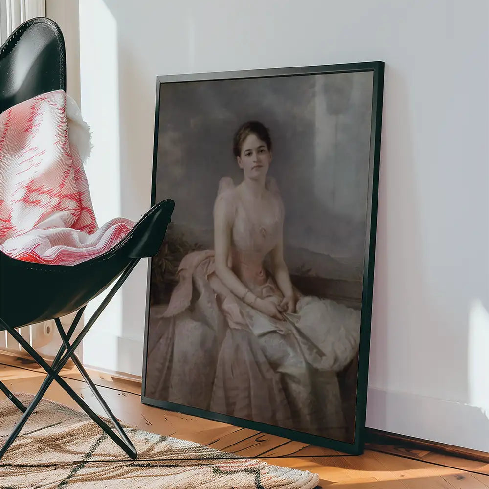 Framed portrait of a woman in a pink gown displayed beside a black chair with a blanket on a wooden floor.