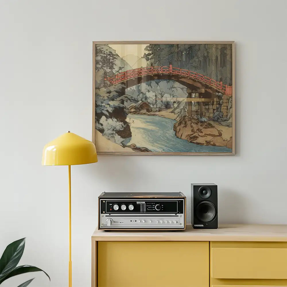 Framed painting of a red bridge over a river, displayed above a yellow lamp and a vintage audio system on a wooden cabinet.