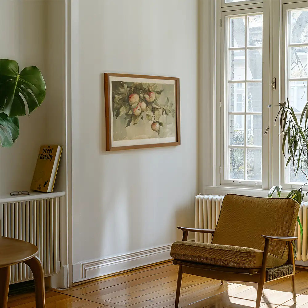 A vintage-style framed painting of apples hanging on a wall in a cozy room with a chair and a plant.