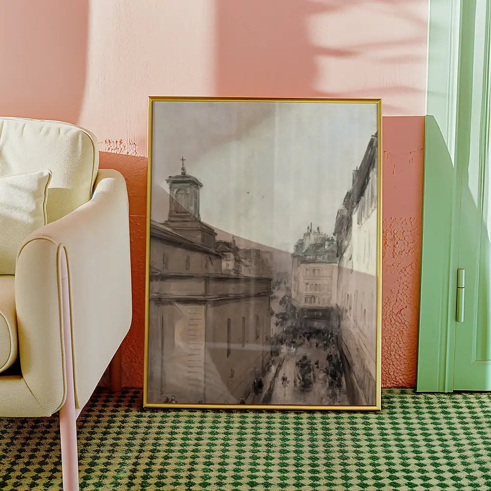 Framed painting of a city street scene displayed beside a light-colored armchair on a green patterned rug.