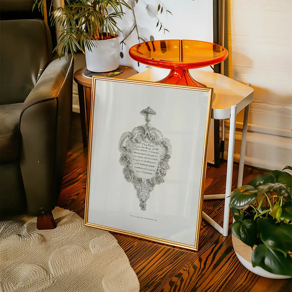 Framed vintage artwork with decorative frame leaning against a chair in a stylish living room setting.