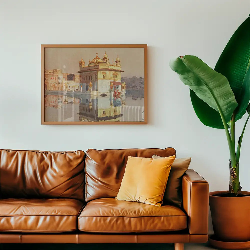 Framed painting of a historical building reflecting in water, displayed above a brown leather sofa with a yellow pillow and a large green plant nearby.