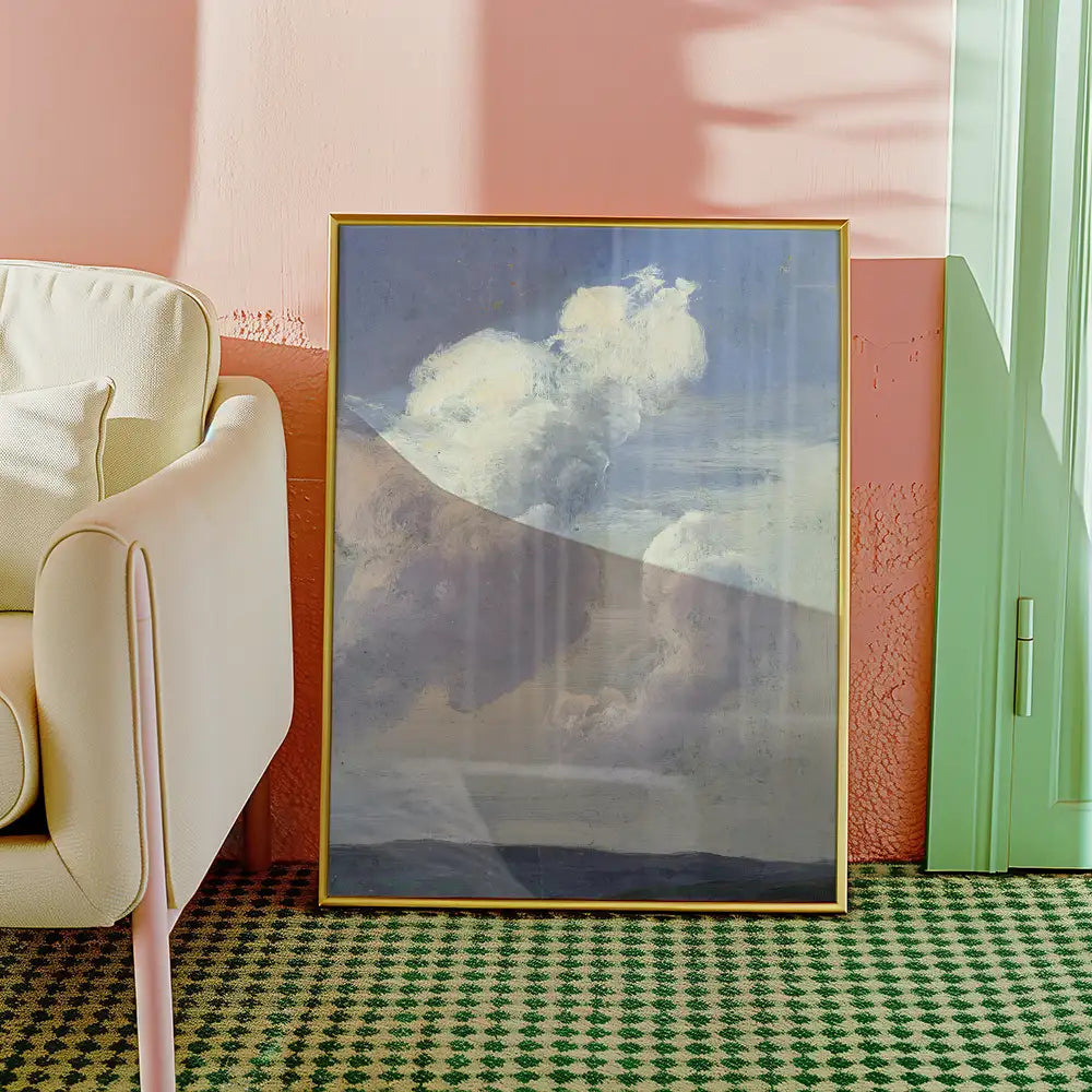 Framed painting of clouds displayed against a pastel pink wall, beside a light-colored armchair on a patterned green rug.