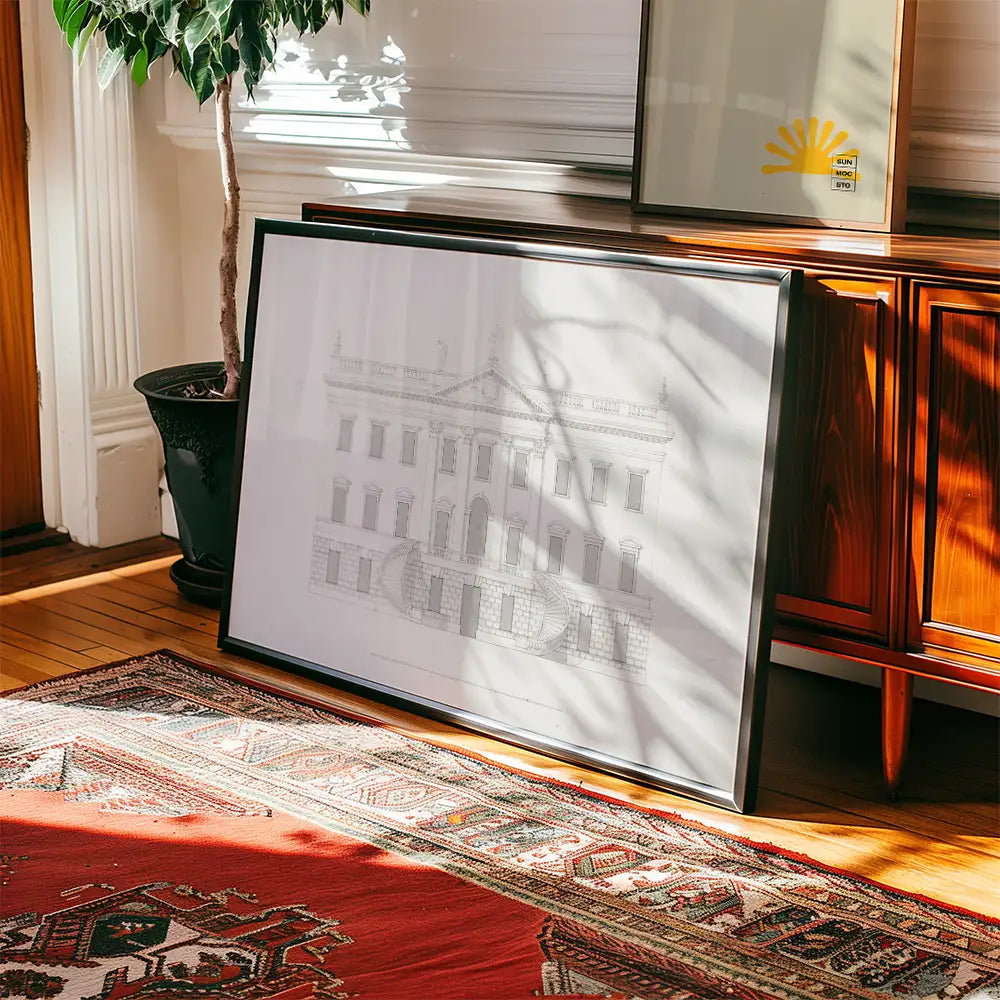 Framed architectural sketch painting leaning against a wooden cabinet with a plant nearby and a patterned rug on the floor.