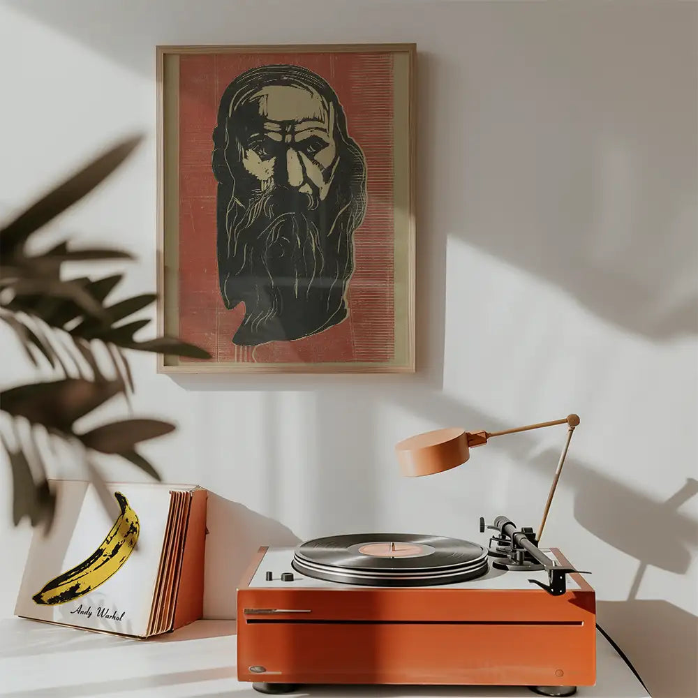 Framed painting of a portrait with a bearded figure in black on a red background, displayed above an orange turntable with a lamp and vinyl records nearby.