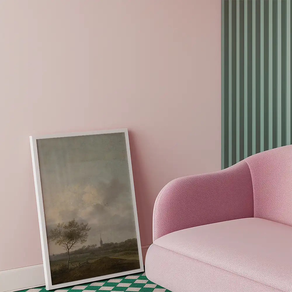 Framed landscape painting leaning against a pink wall next to a modern pink sofa with textured fabric.
