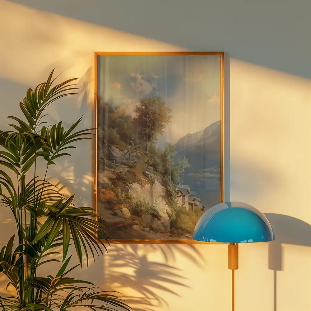 Framed landscape painting depicting a serene mountain view, accompanied by a green plant and a modern blue lamp against a softly lit wall.