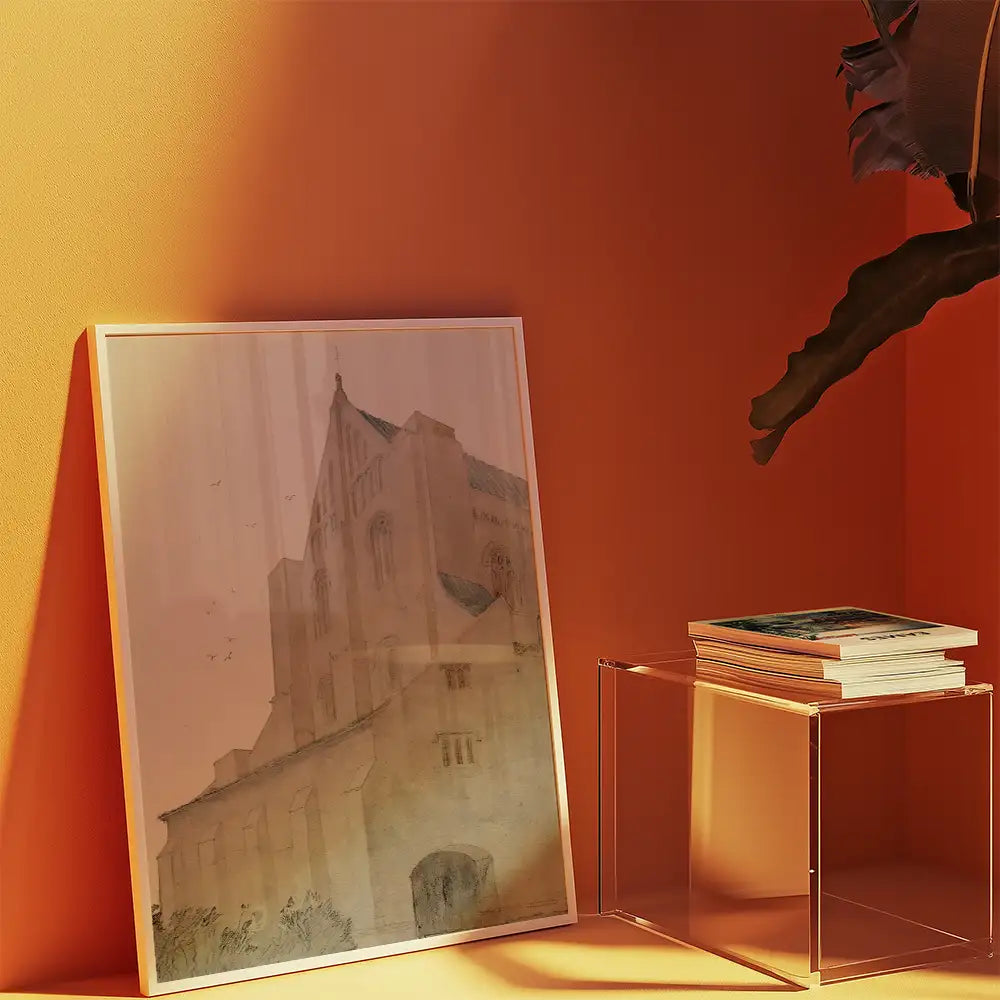 Framed watercolor painting of a building leaning against a textured orange wall, with a clear side table holding stacked books nearby.