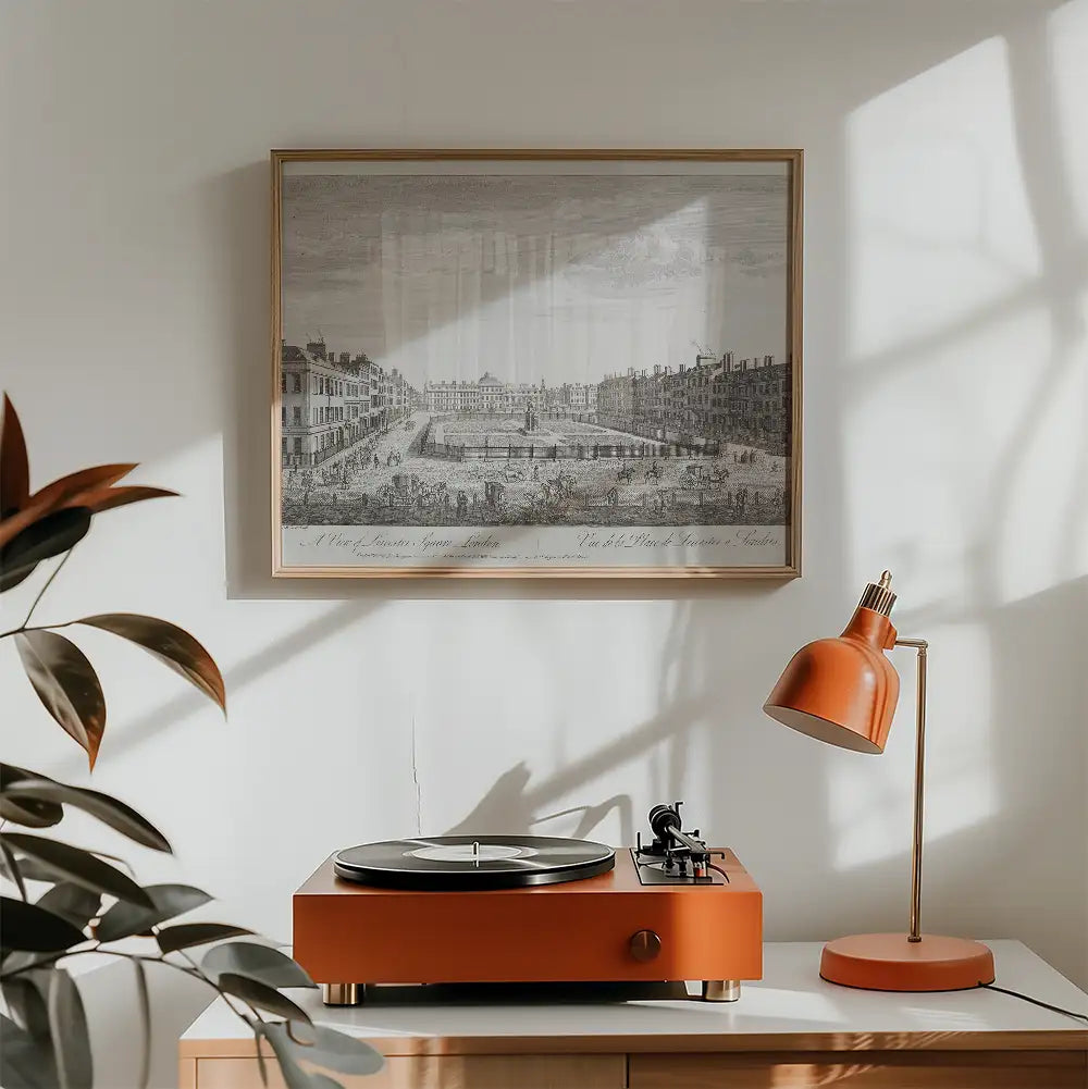 Vintage-style frame displaying an intricate black and white cityscape poster above an orange turntable and matching desk lamp, set in a modern living space with natural light and greenery.