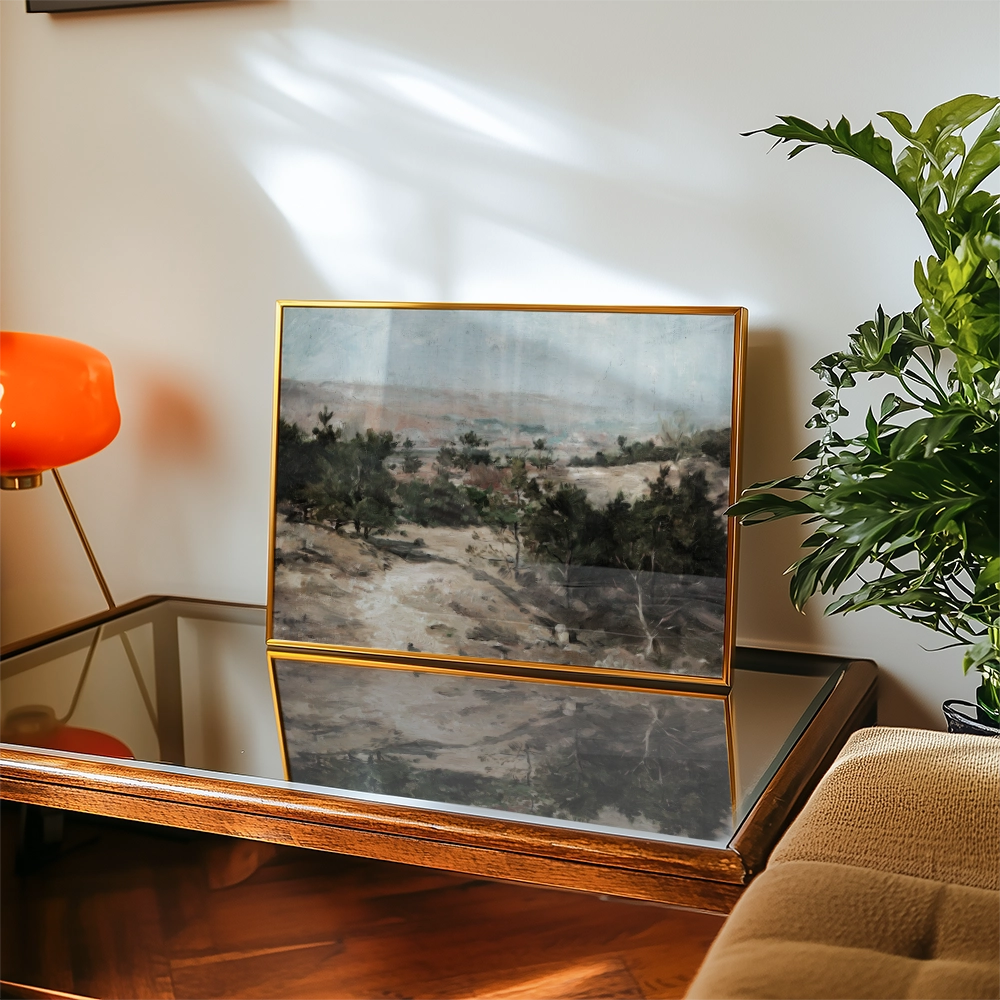 Framed landscape painting displayed on a glass coffee table with a decorative lamp and indoor plant in a cozy living room setting.