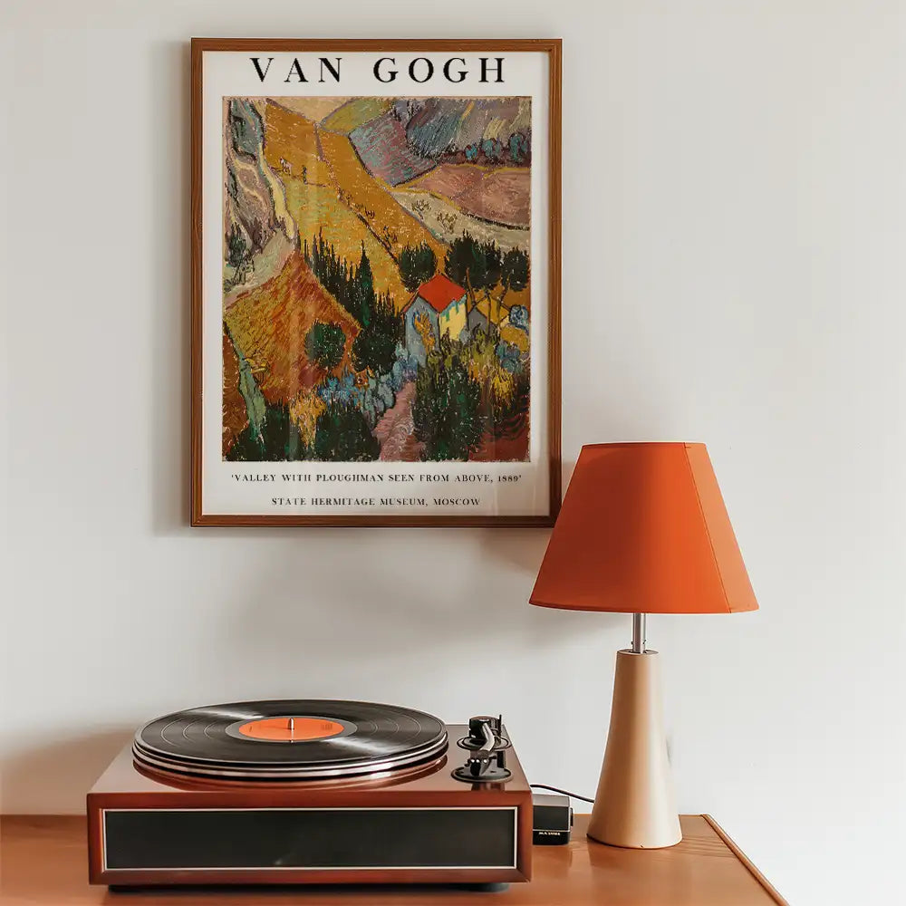 Vincent van Gogh poster titled "Valley with Ploughman Seen from Above, 1889" framed on a wall next to a record player and an orange lamp.