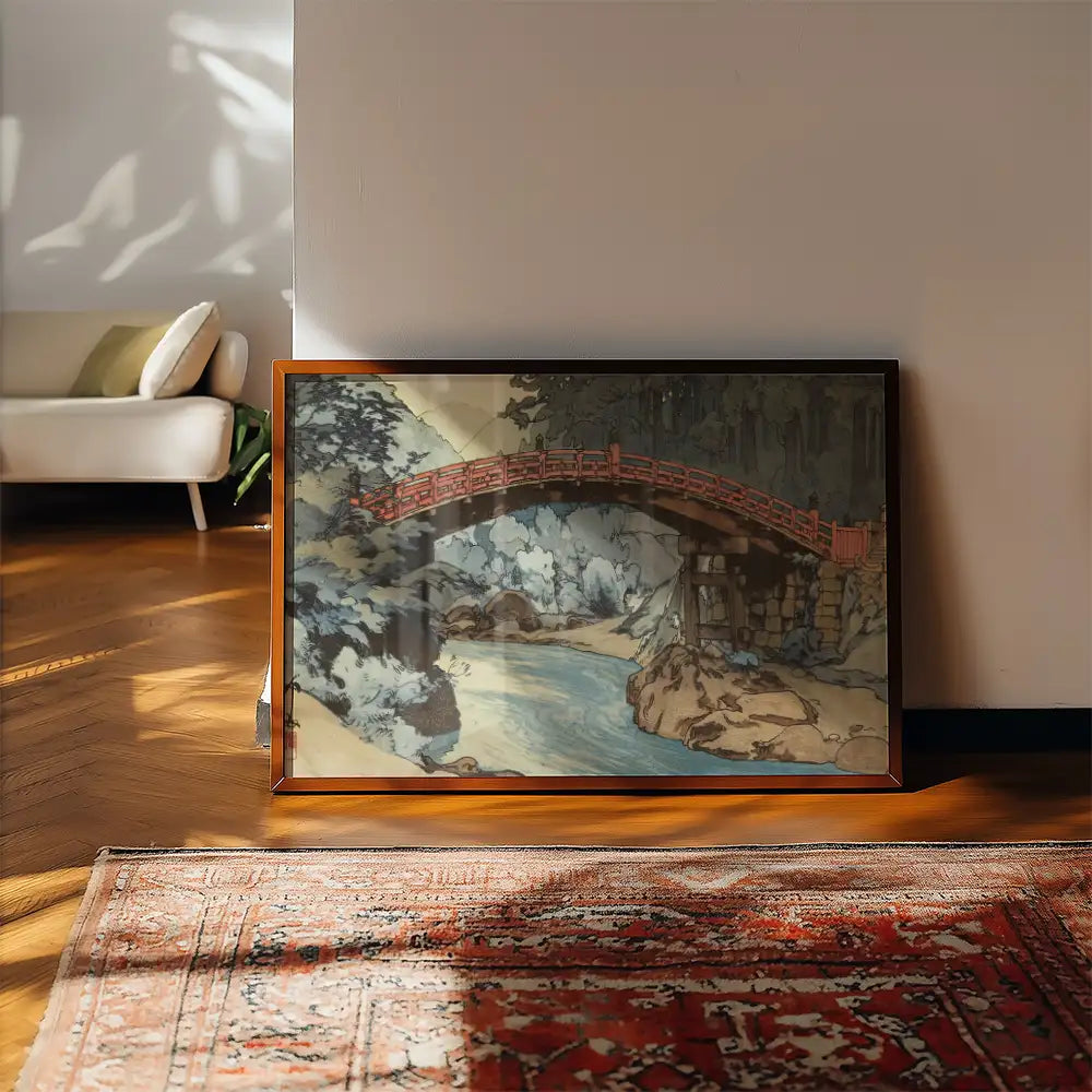 Framed painting of a red bridge over a river surrounded by trees, displayed in a bright interior setting.