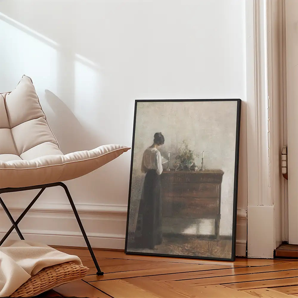 Framed painting of a woman standing by a dresser with flowers, leaning slightly forward, in a softly lit room with wooden flooring and a modern chair.
